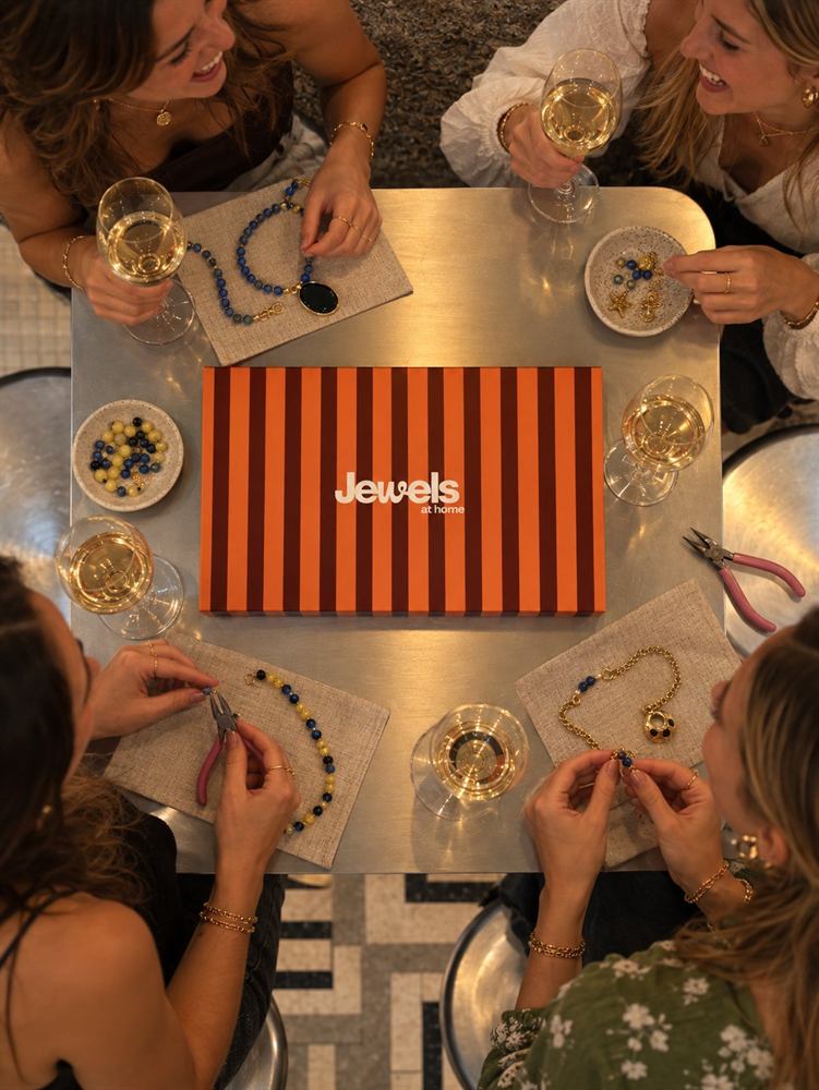 Amigas creando joyas alrededor de una mesa con la caja JEWELSathome y copas de vino